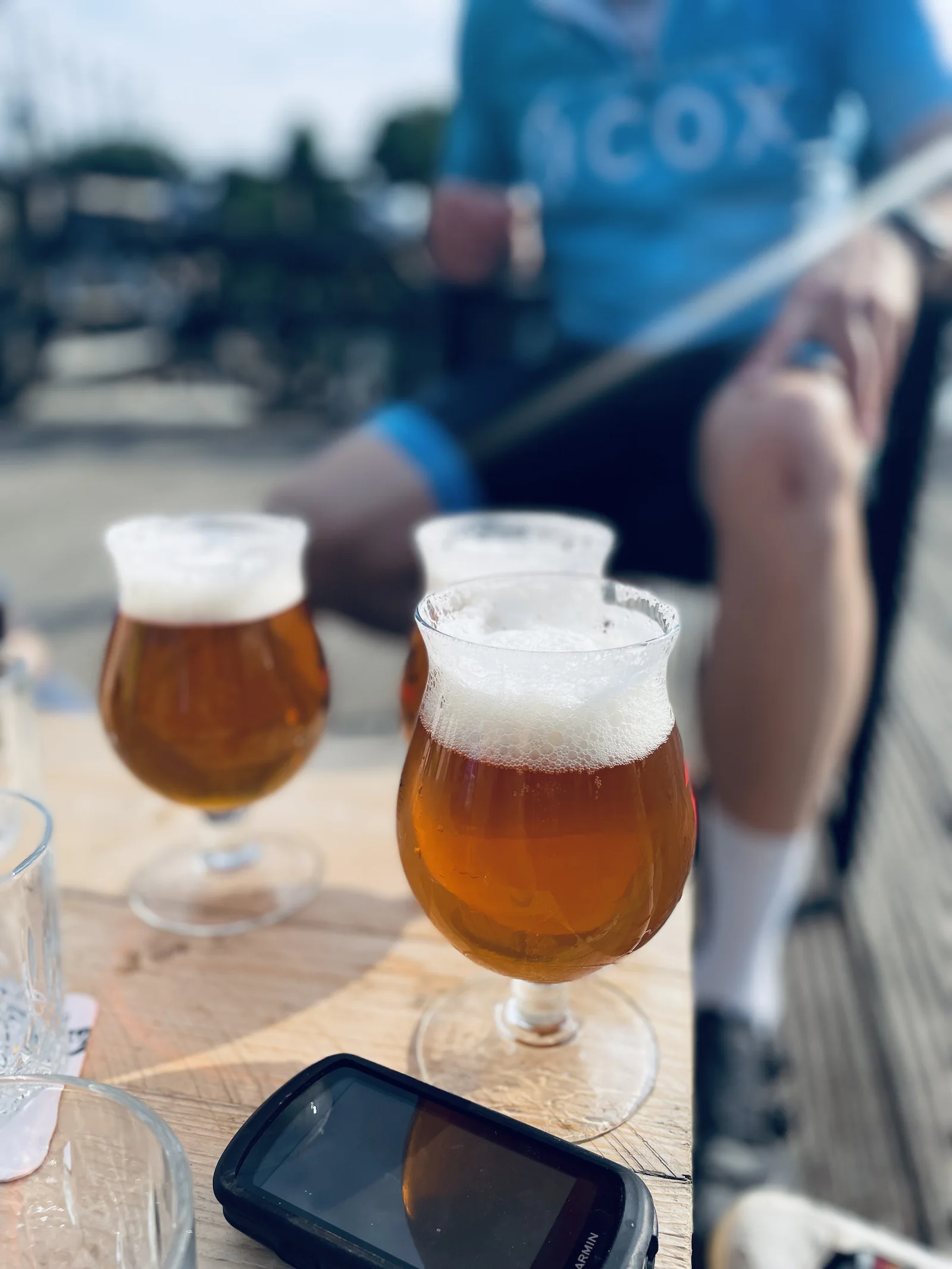 Bierglazen na een Ride2Connect-rit met een fietser in clubtenue op de achtergrond